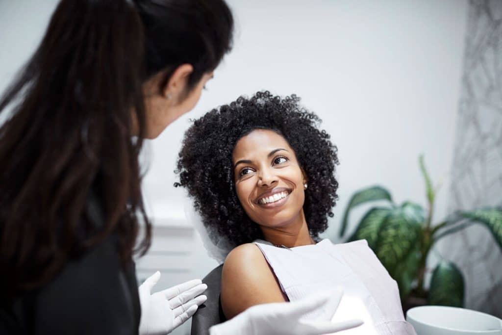 Woman in dental chair smiling and having a discussion with dentist